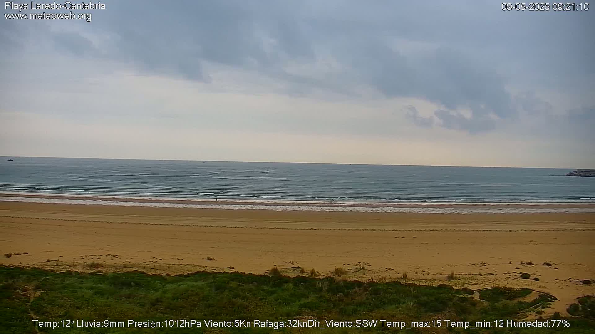 A wide sandy beach stretches to a calm ocean under an overcast sky.
