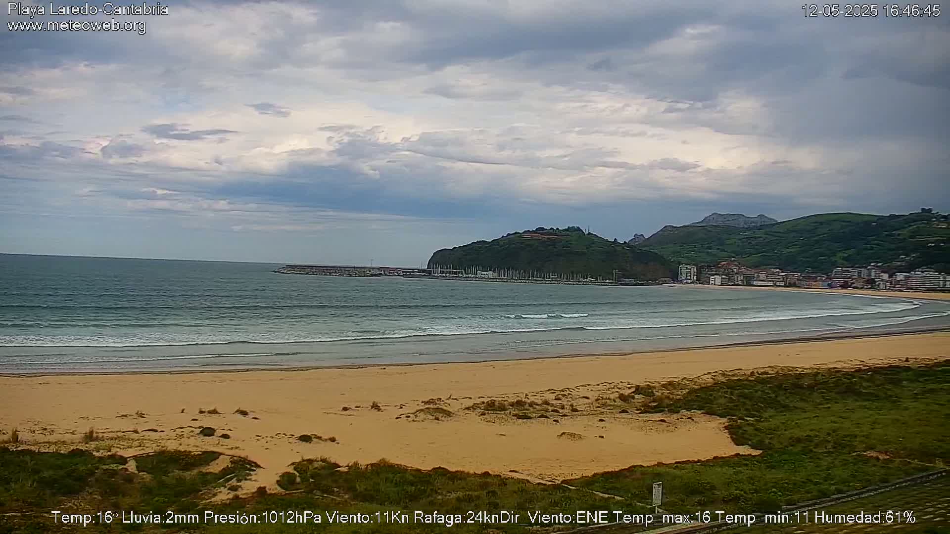 A sandy beach with small waves laps a shore under a mostly cloudy sky.