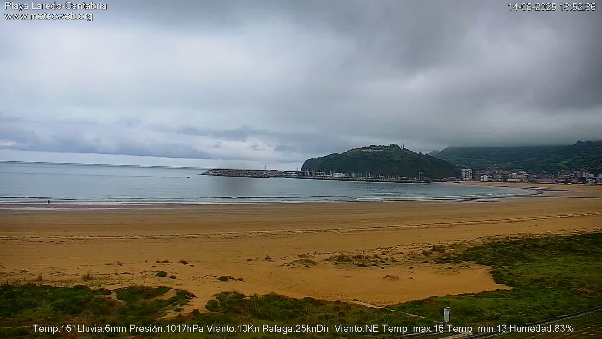 A wide sandy beach stretches out to a calm sea under a cloudy sky.