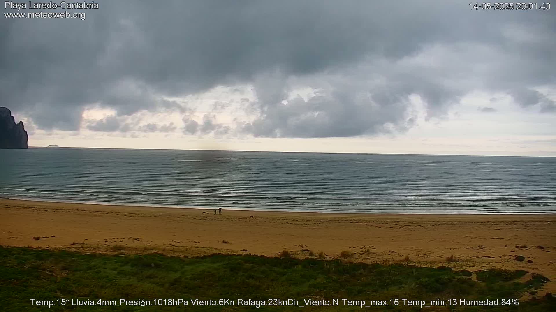 A sandy beach stretches to a calm sea under an overcast sky.