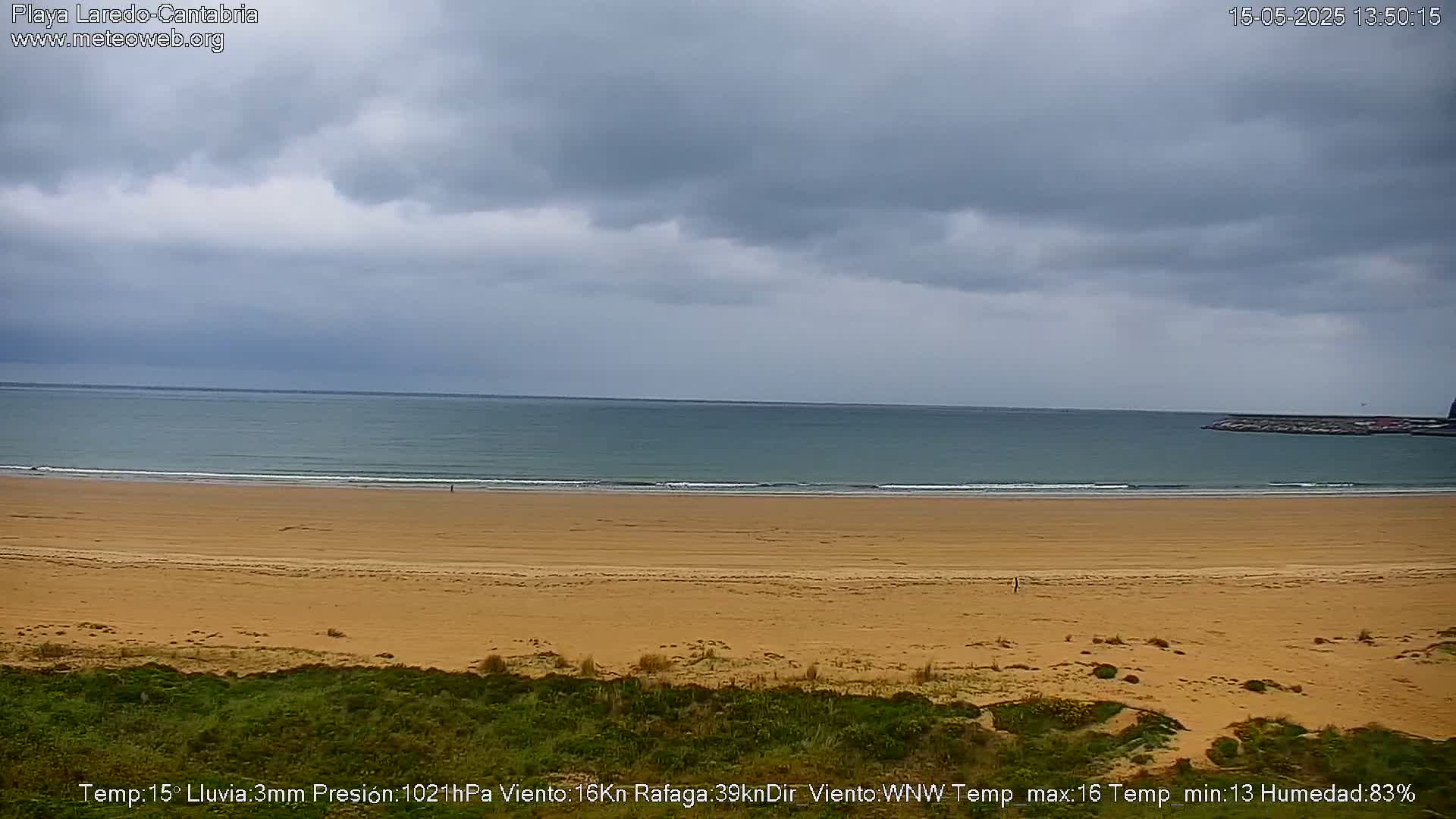 A wide sandy beach stretches to a calm sea under a cloudy sky.