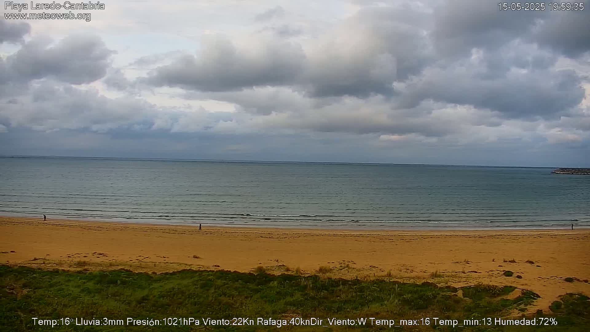 A sandy beach and calm ocean are visible under a cloudy sky.