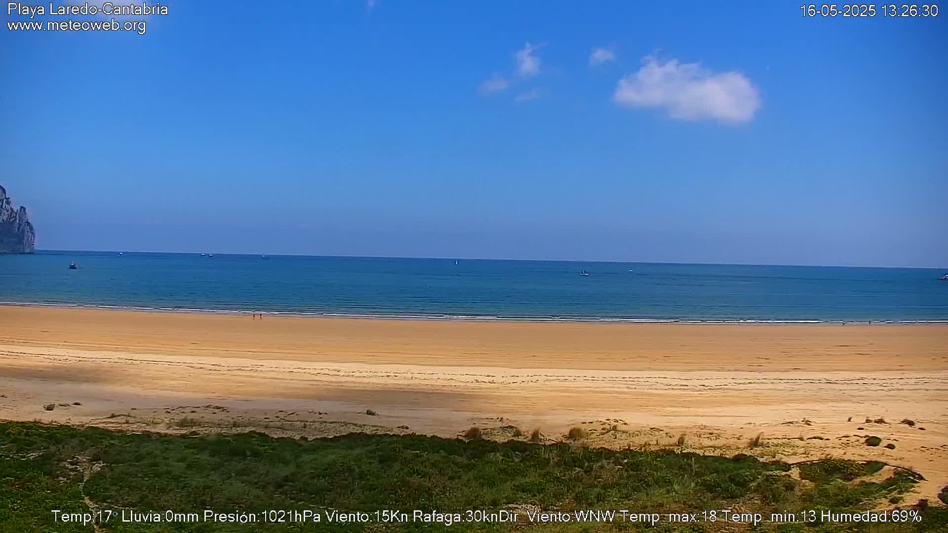 A sandy beach stretches to a calm, blue ocean under a mostly clear sky, with a distant rocky outcrop visible to the left.