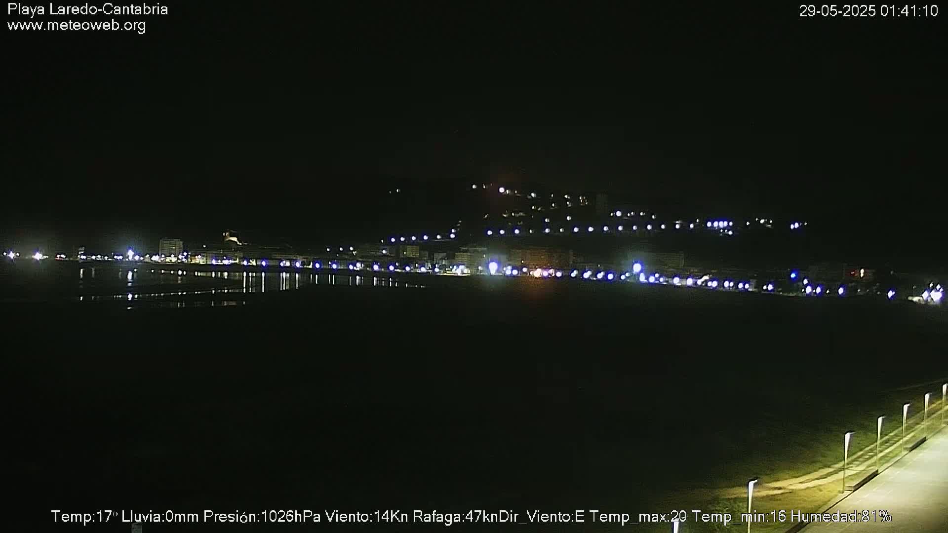 A nighttime view of a coastal town with lights reflecting on a calm body of water.