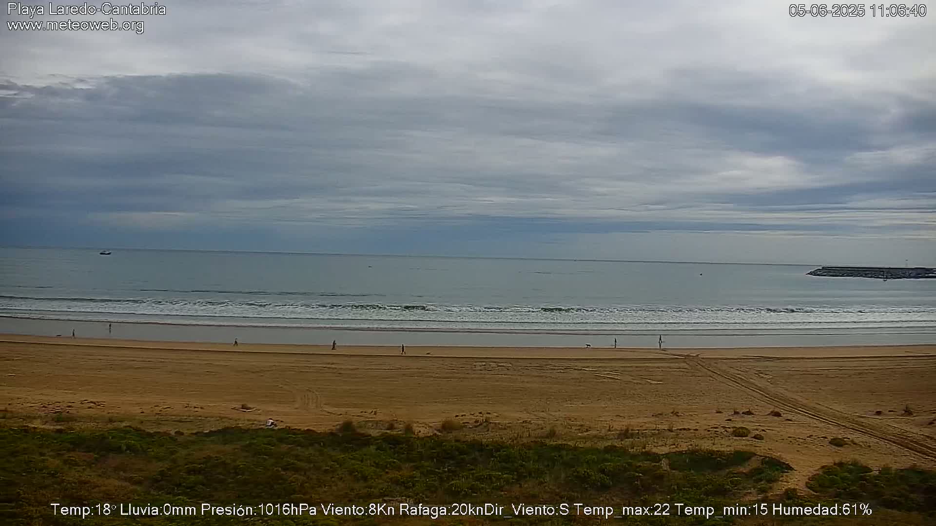 A wide, sandy beach stretches to a calm ocean under a mostly cloudy sky.
