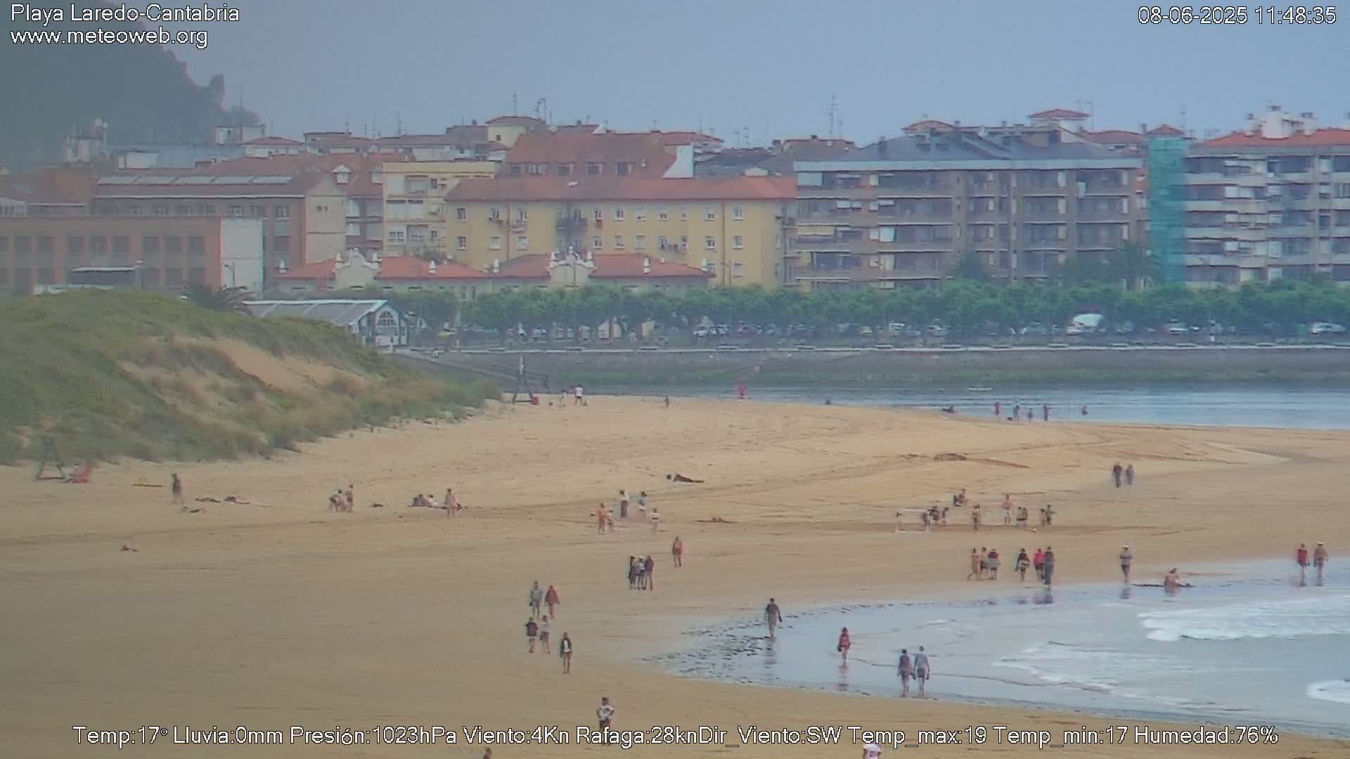 A sandy beach with a few people scattered across it and a calm body of water, all under an overcast sky.