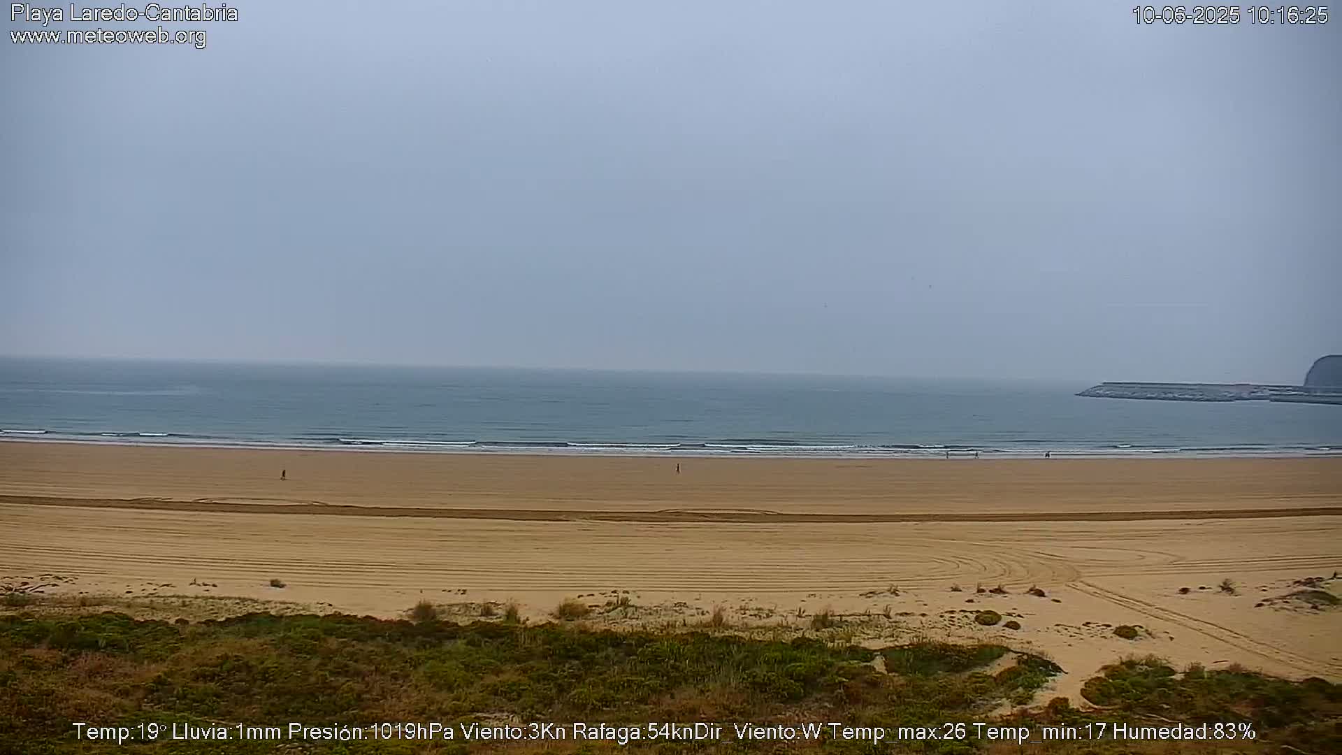A wide, sandy beach stretches to a calm, gray ocean under an overcast sky.