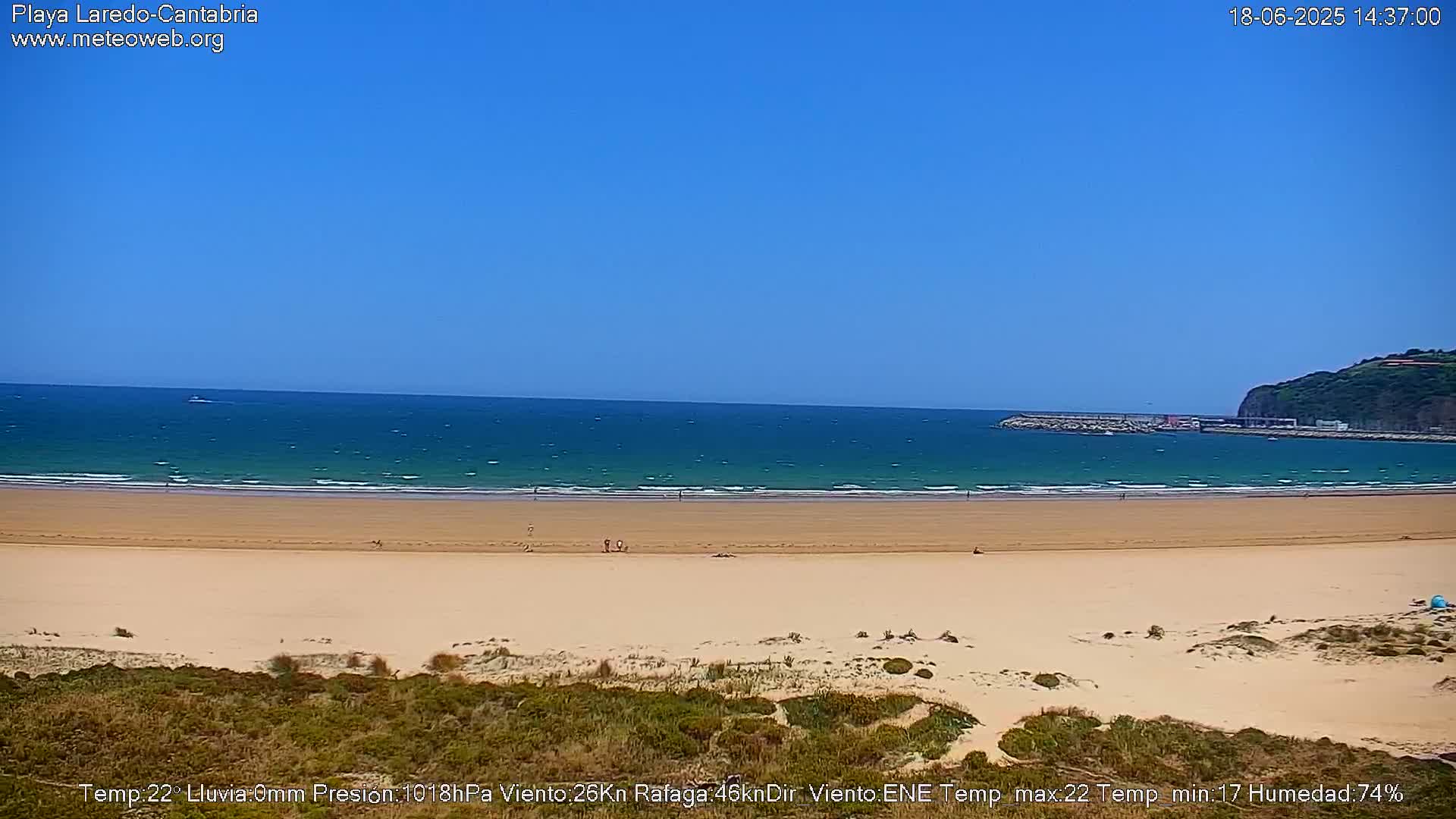 A sandy beach stretches to a calm, teal ocean under a clear blue sky.