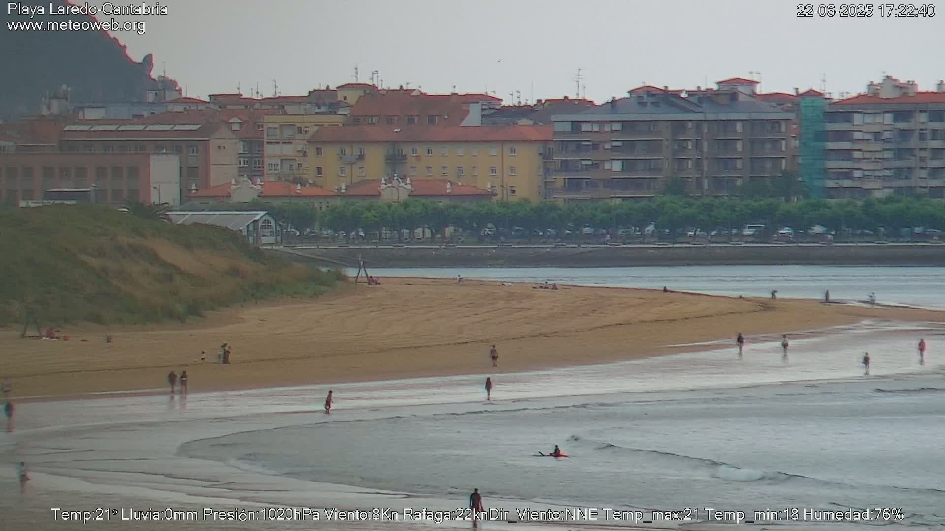 A sandy beach with a few people on it and gentle waves rolling in under an overcast sky.