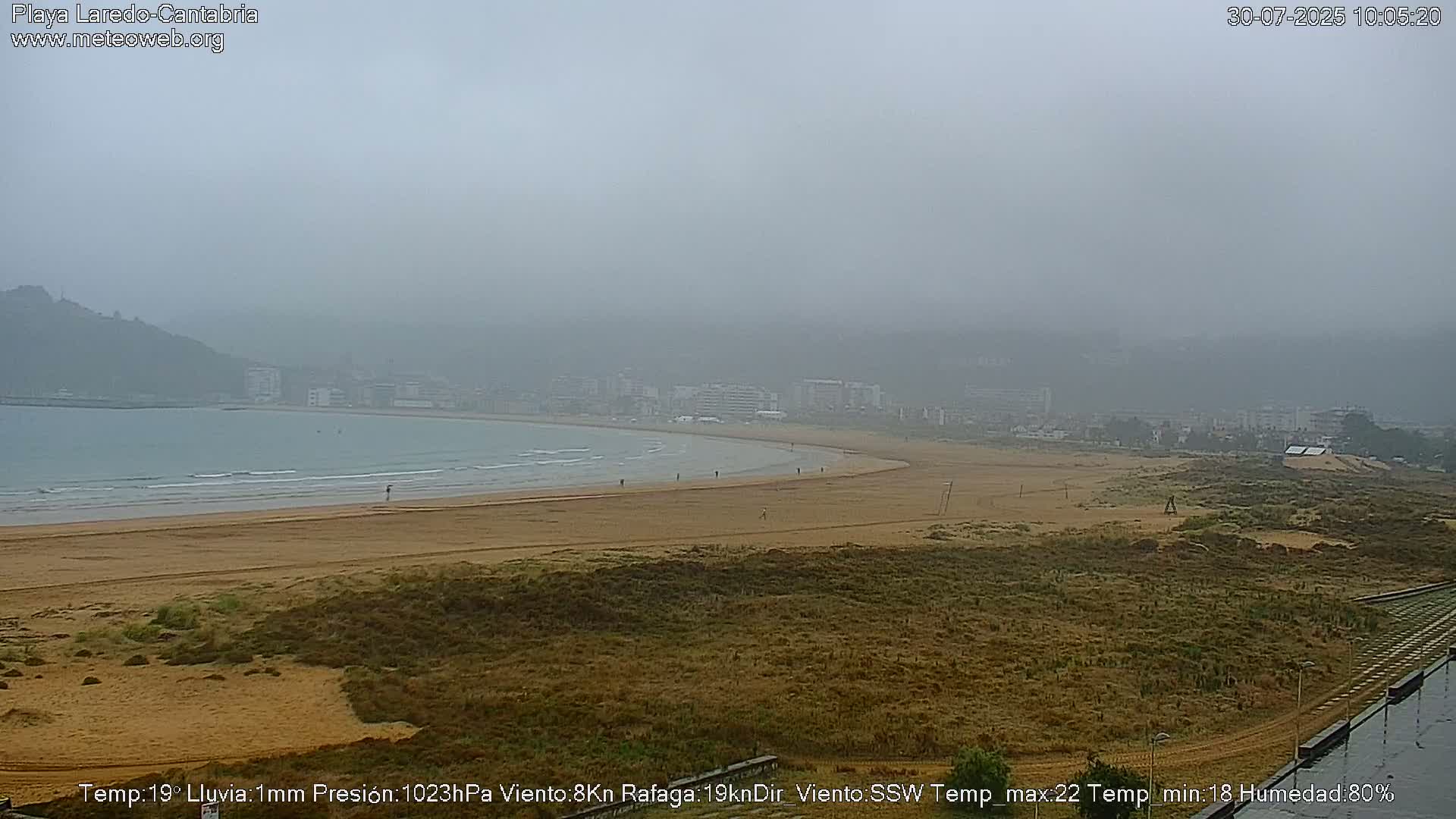 A foggy view of a sandy beach with a town in the background and a calm sea.