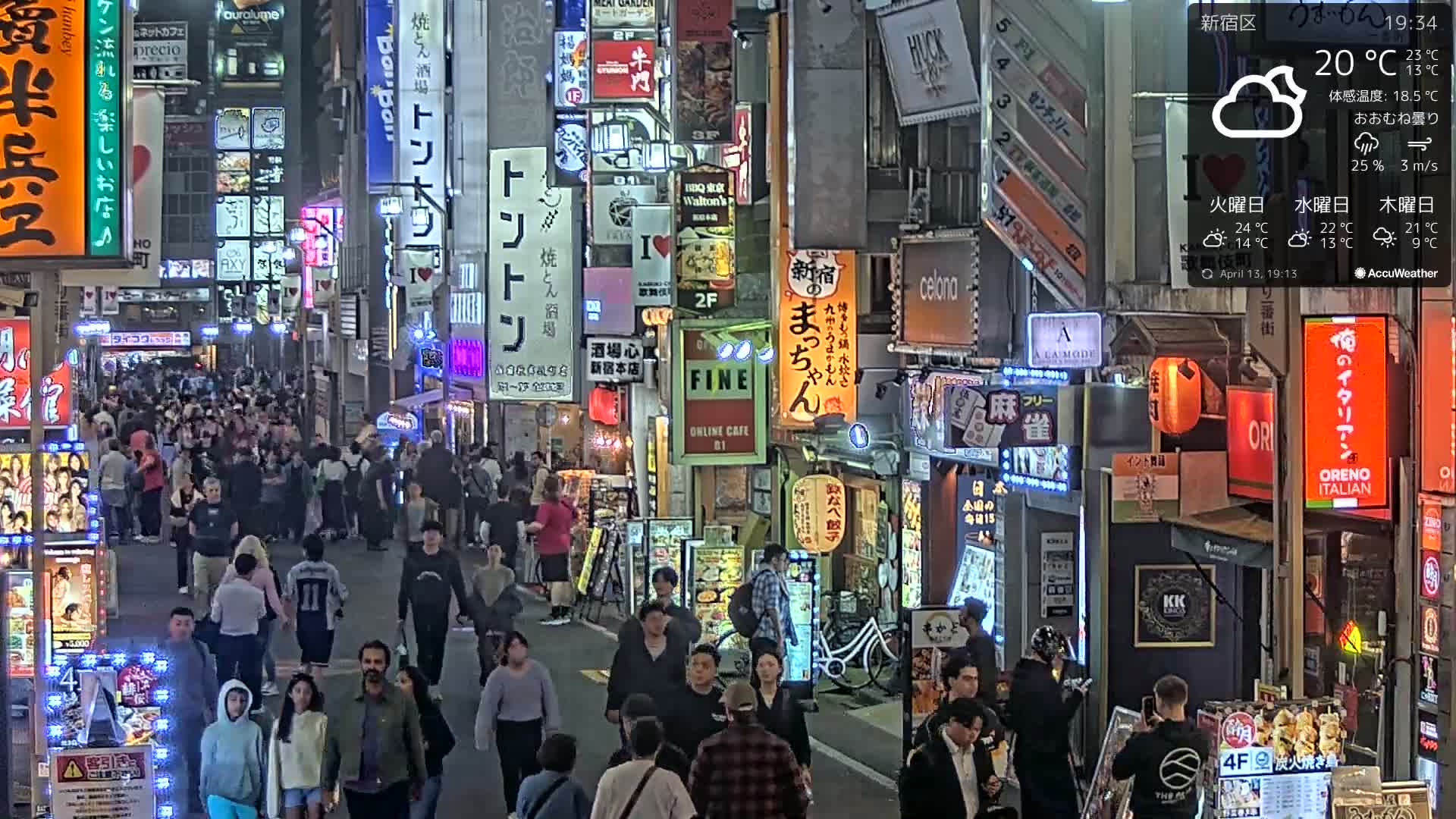 A dense crowd of people walks along a brightly lit city street at night, flanked by buildings covered in numerous colorful illuminated signs, under clear weather conditions with a temperature of 8°C.