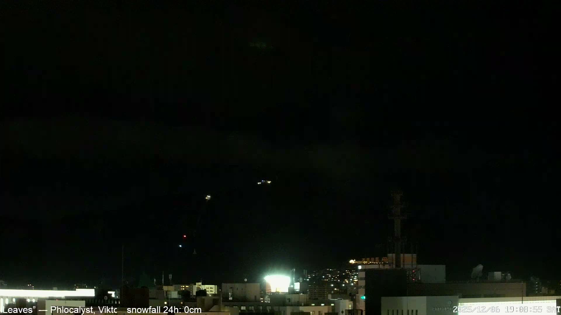 A clear, dark night sky hangs over a cityscape dotted with numerous illuminated buildings and streets, with a few bright, distant lights visible high above.
