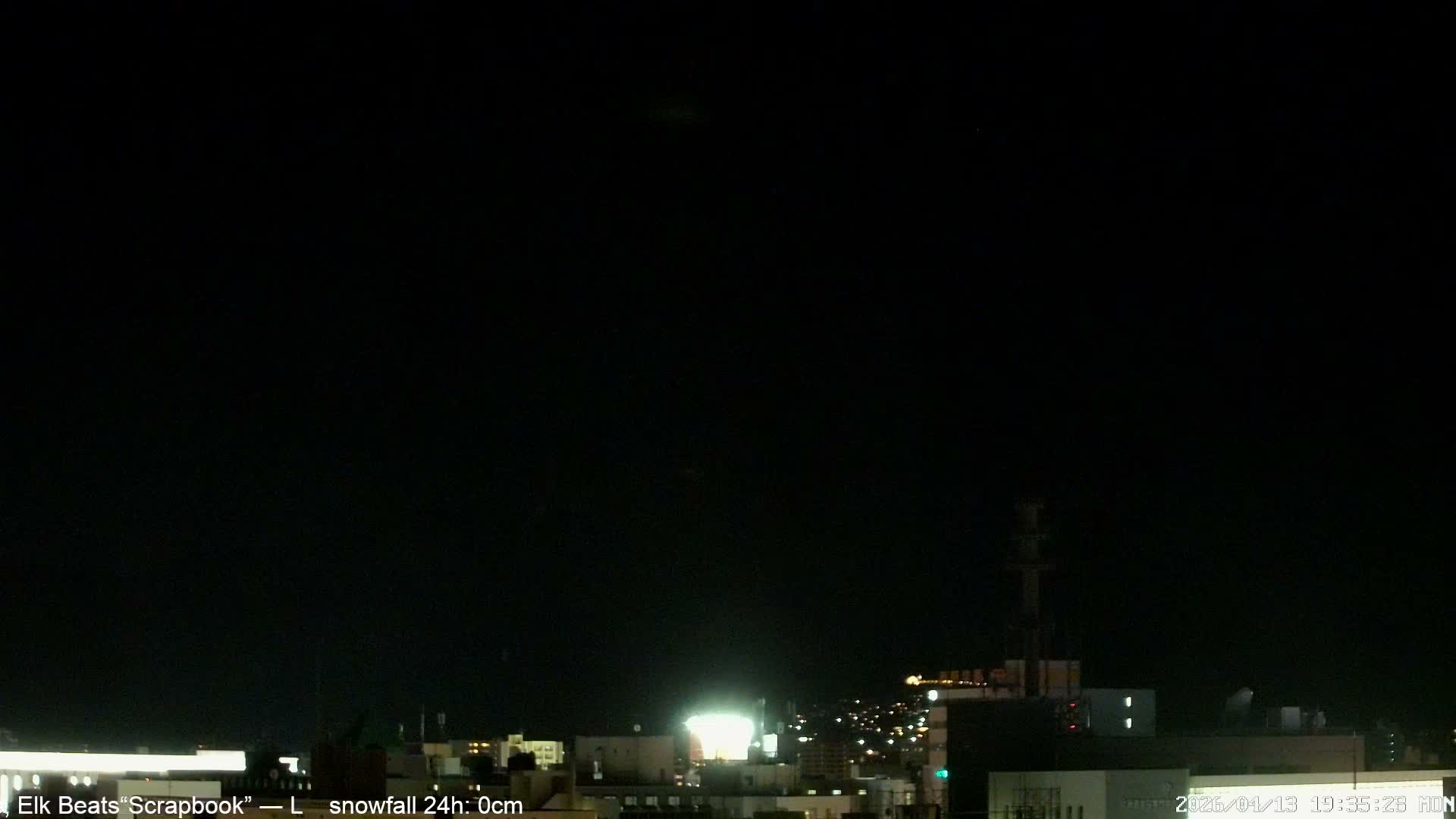 A clear, dark night sky hangs over a cityscape dotted with numerous illuminated buildings and streets, with a few bright, distant lights visible high above.