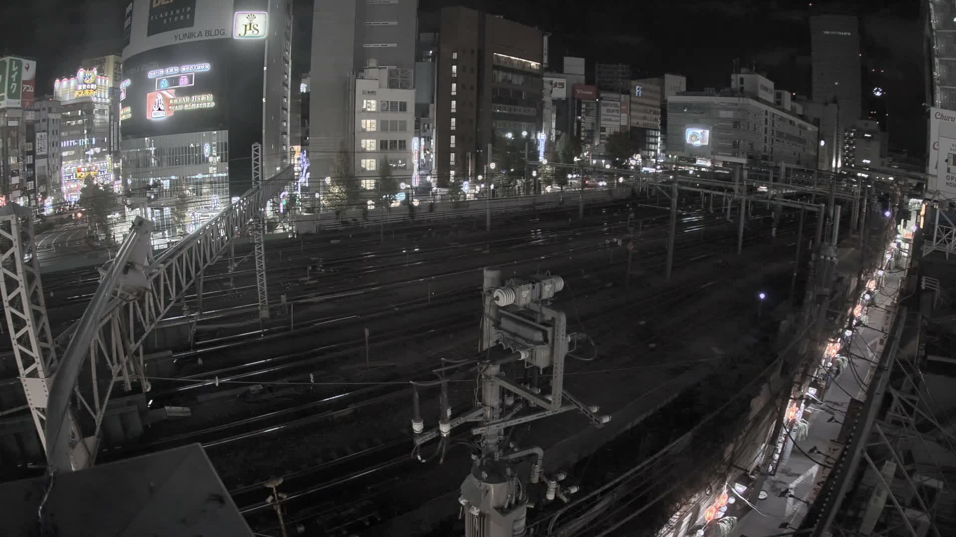 An elevated nighttime view showcases numerous parallel train tracks in an urban setting, surrounded by brightly lit buildings under a clear sky.