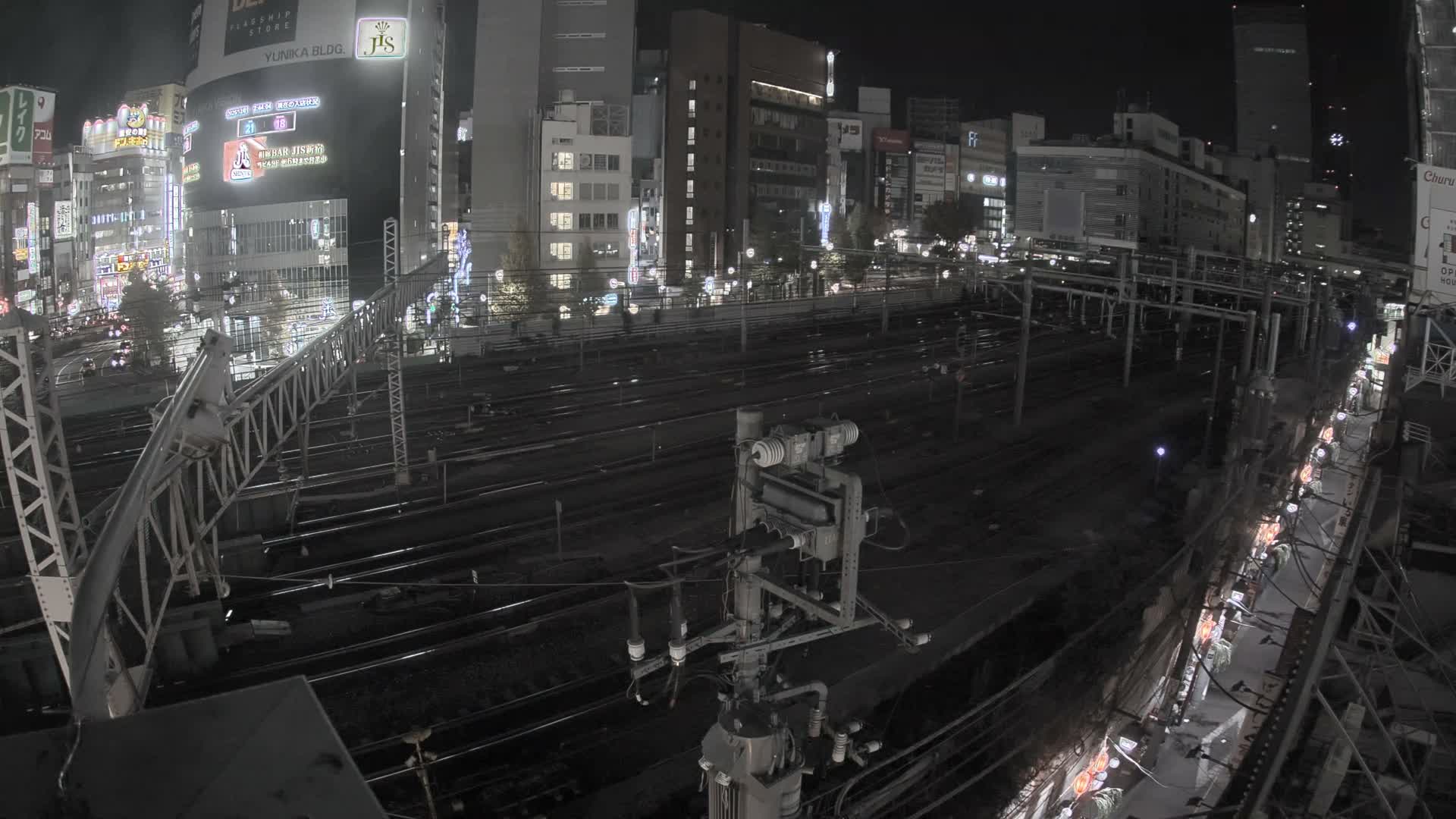 An elevated nighttime view showcases numerous parallel train tracks in an urban setting, surrounded by brightly lit buildings under a clear sky.