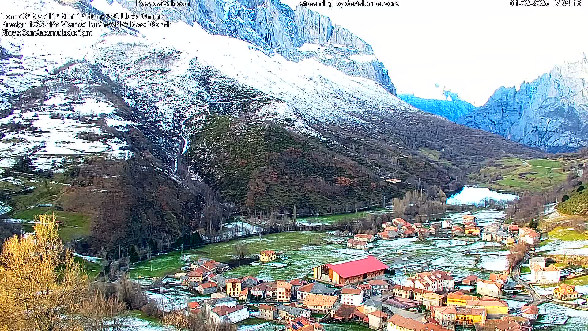 A small village nestled in a valley between snow-dusted mountains, under a mostly clear sky.