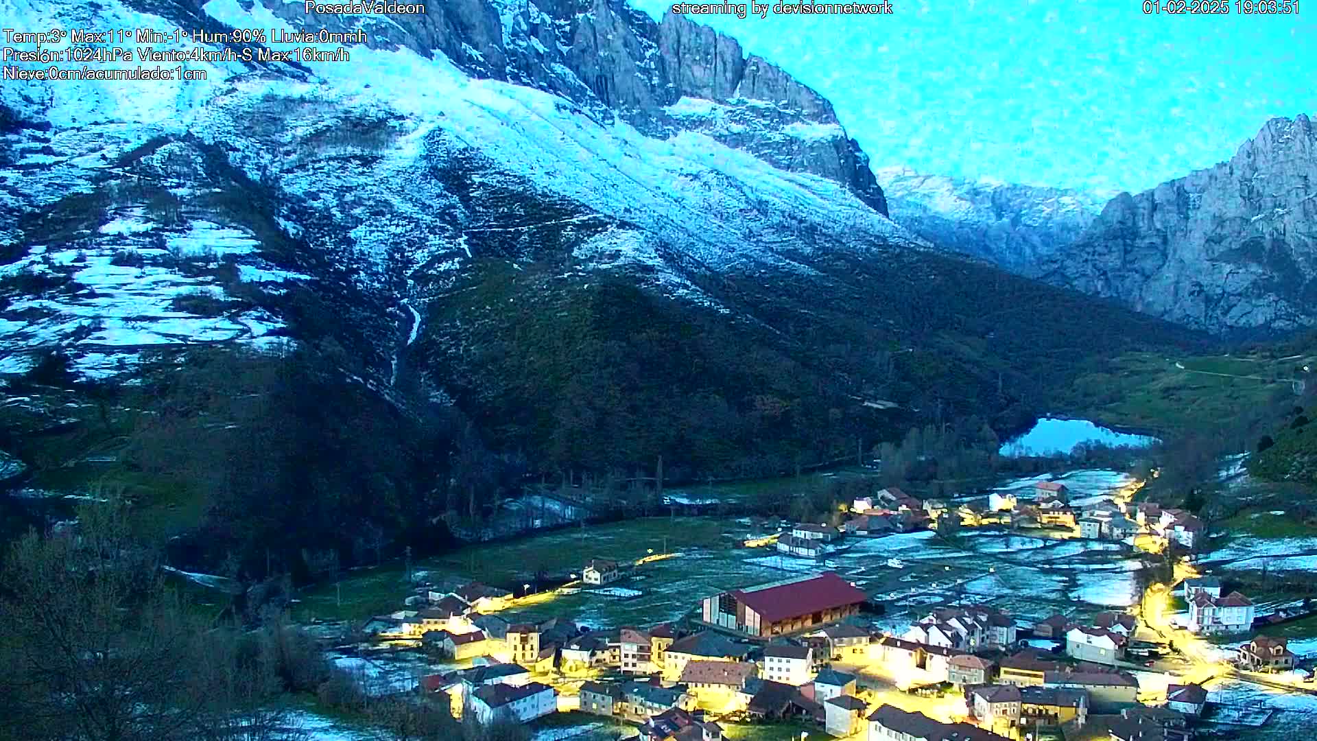 A small, snow-dusted village nestled in a valley between towering, snow-capped mountains at twilight.