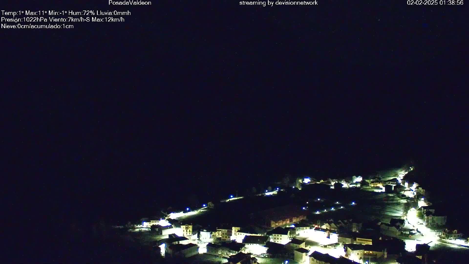A nighttime, aerial view of a small, snow-covered town illuminated by streetlights under a clear, dark sky.