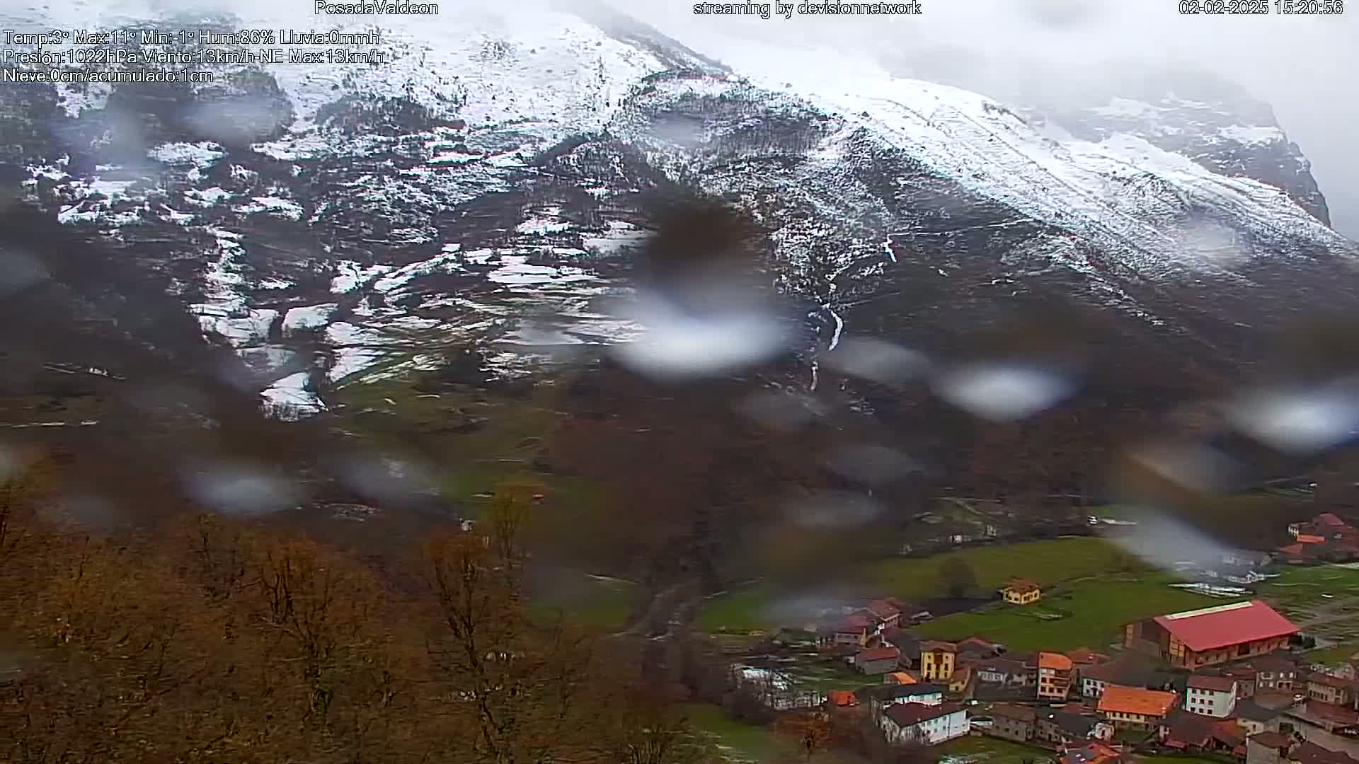 Rain falls on a snow-dusted mountain overlooking a small village nestled in a valley.