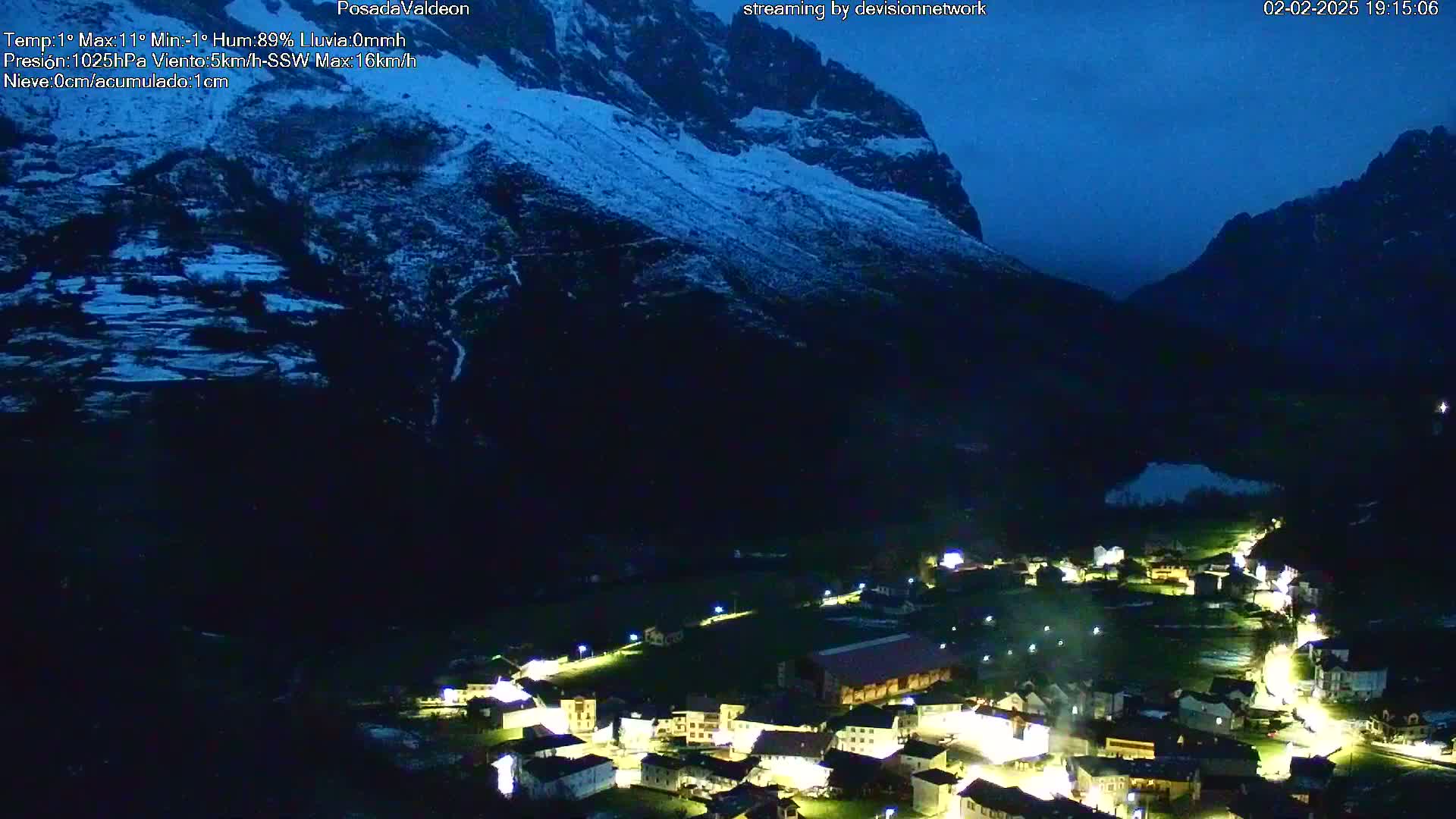 A small, illuminated village nestled in a valley between snow-dusted mountains under a dark, twilight sky.