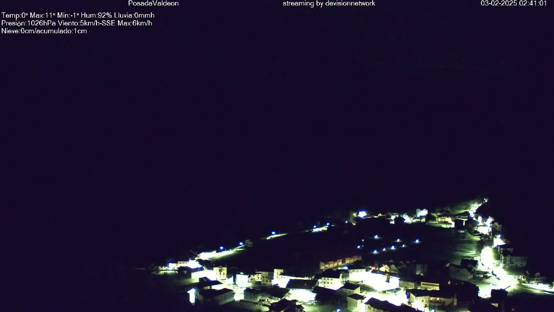 A small, illuminated village is nestled in a dark, nighttime landscape.