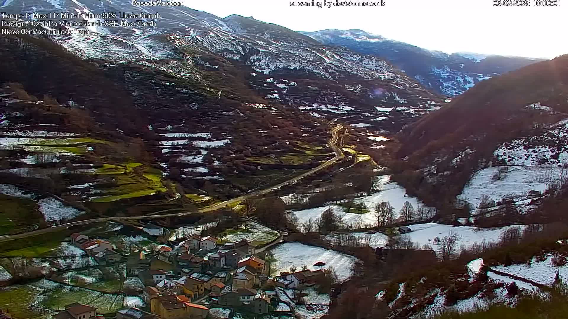 A small village nestled in a snow-dusted valley between mountains, under a sunny sky.