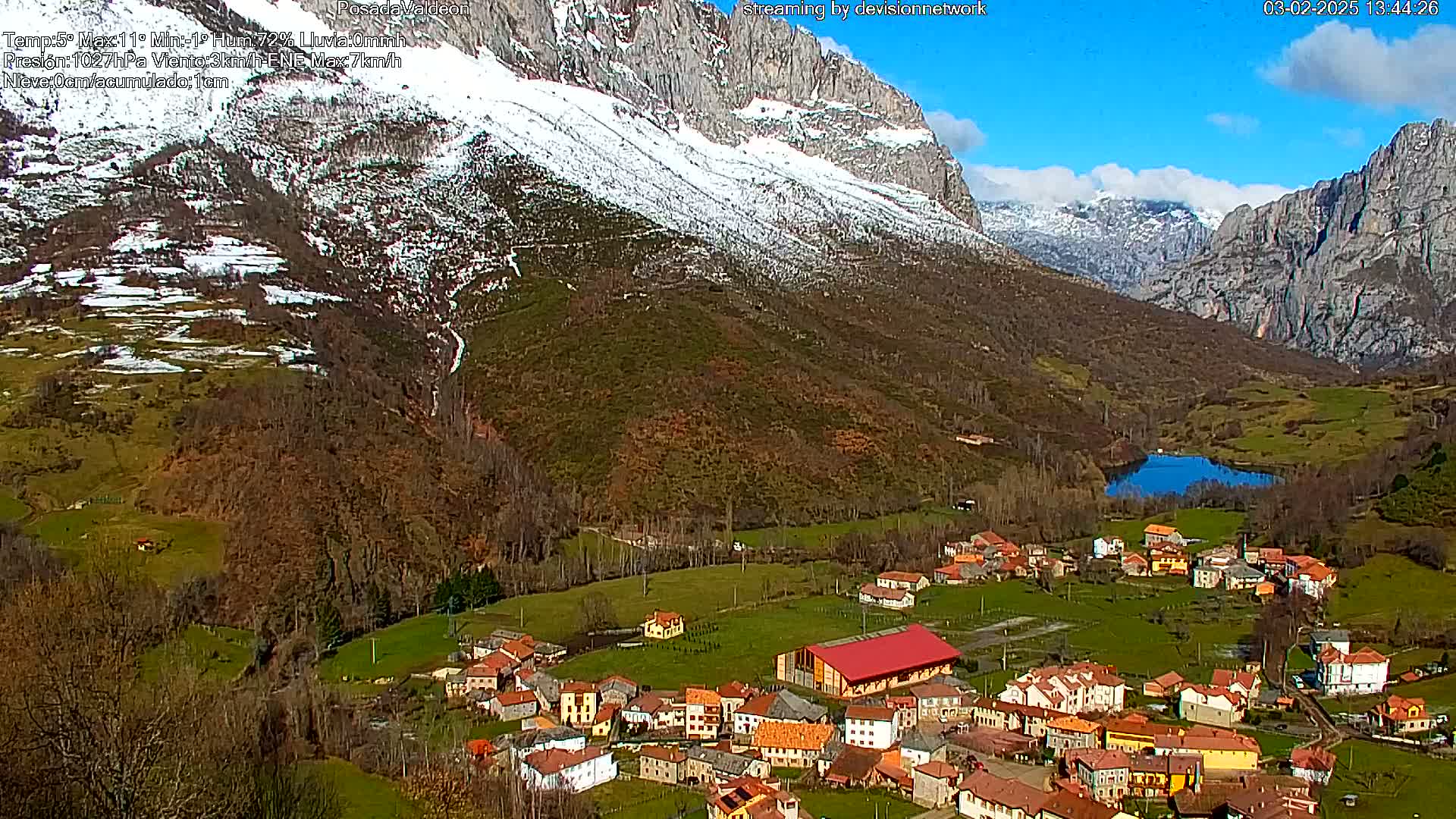 A small village nestled in a valley between snow-capped mountains under a mostly sunny sky.