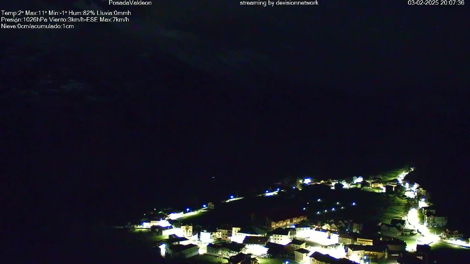 A small, illuminated village is nestled in a dark, nighttime landscape under a mostly clear sky.