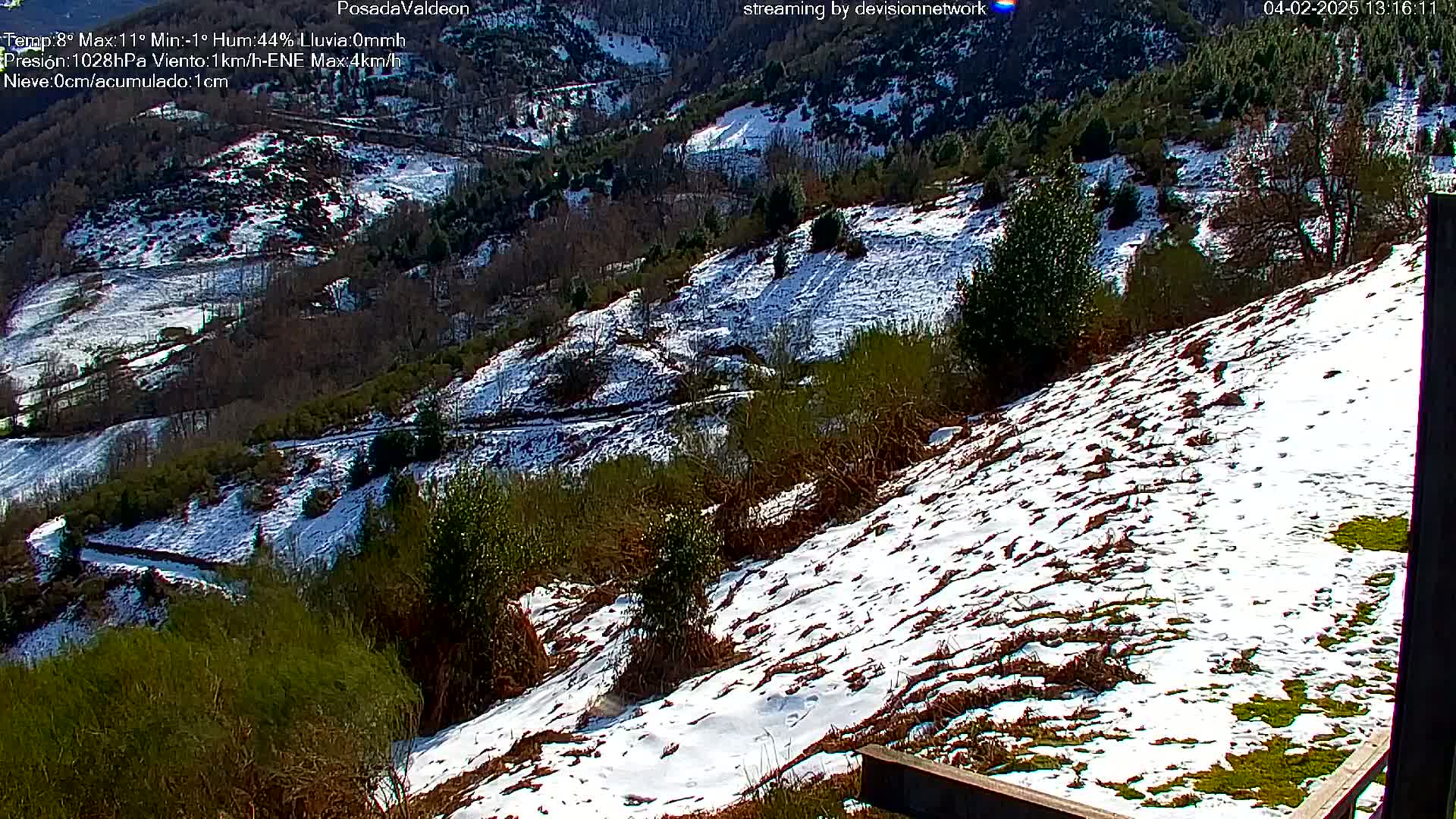 A snow-dusted hillside and valley with dark green vegetation, under a sunny sky.