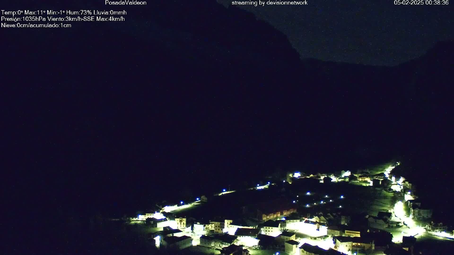 A nighttime, high-angle view of a small, illuminated village nestled beneath a dark mountain, under a clear sky.