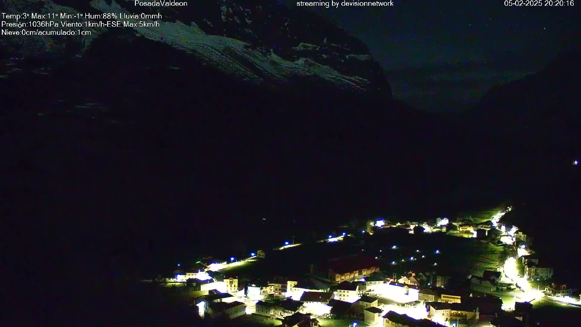 A small, illuminated village nestled at the base of a dark mountain under a clear, starry night sky.