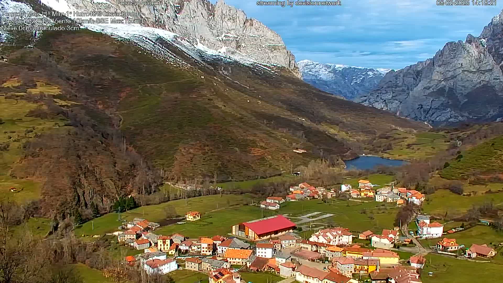 A small village nestled in a valley between snow-dusted mountains under a partly cloudy sky.