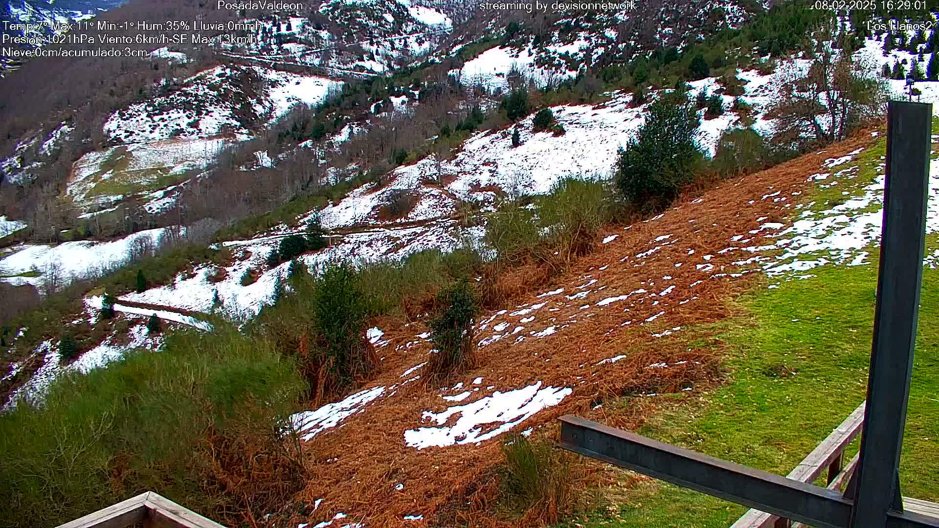 A snow-dusted hillside with patches of brown vegetation and green grass is seen from an elevated vantage point, possibly a viewing platform.