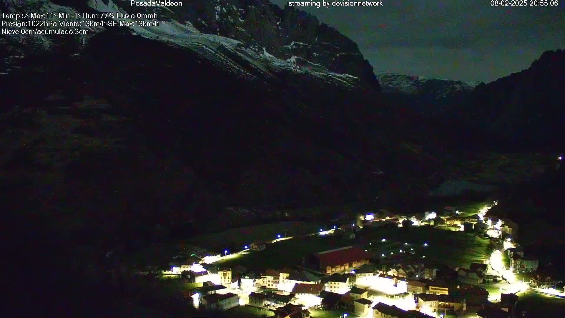 A small, lit village nestled in a dark valley between snow-capped mountains at night.