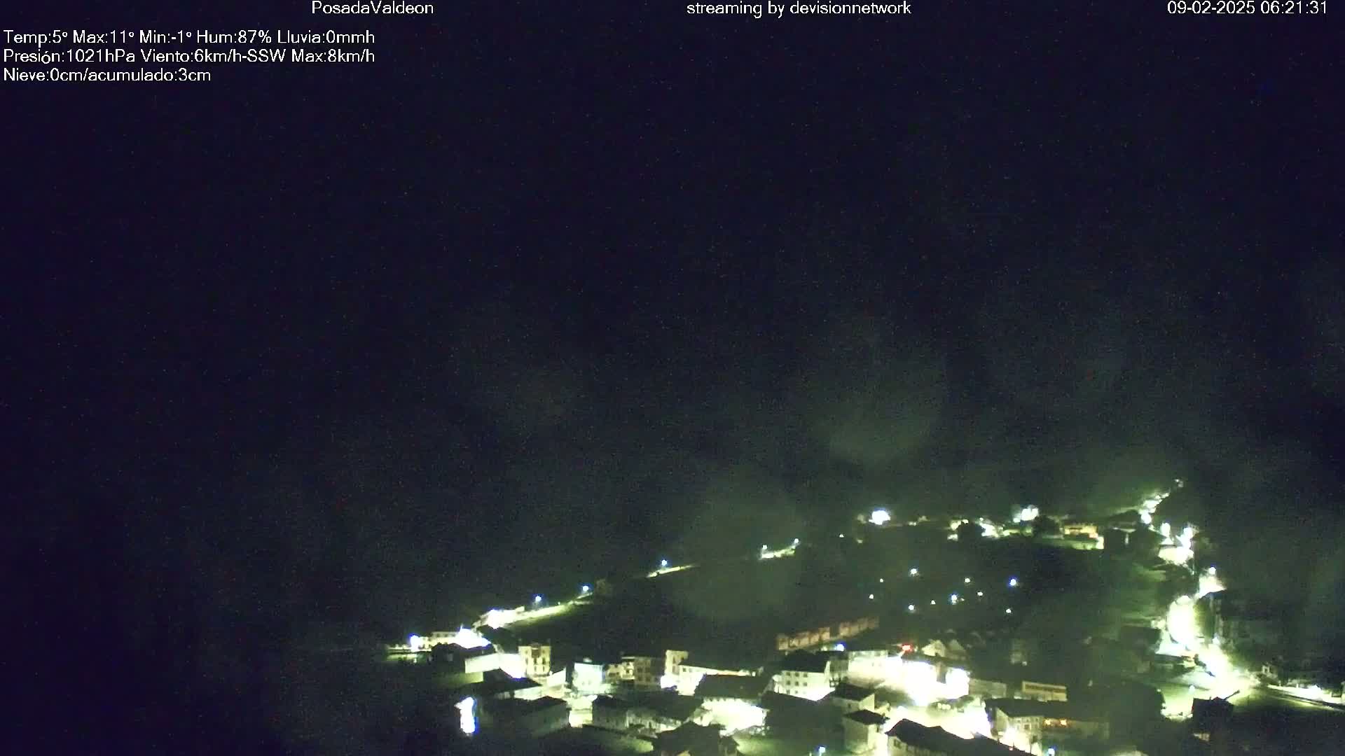 A nighttime, high-angle view of a small village illuminated by lights under a dark, mostly clear sky.