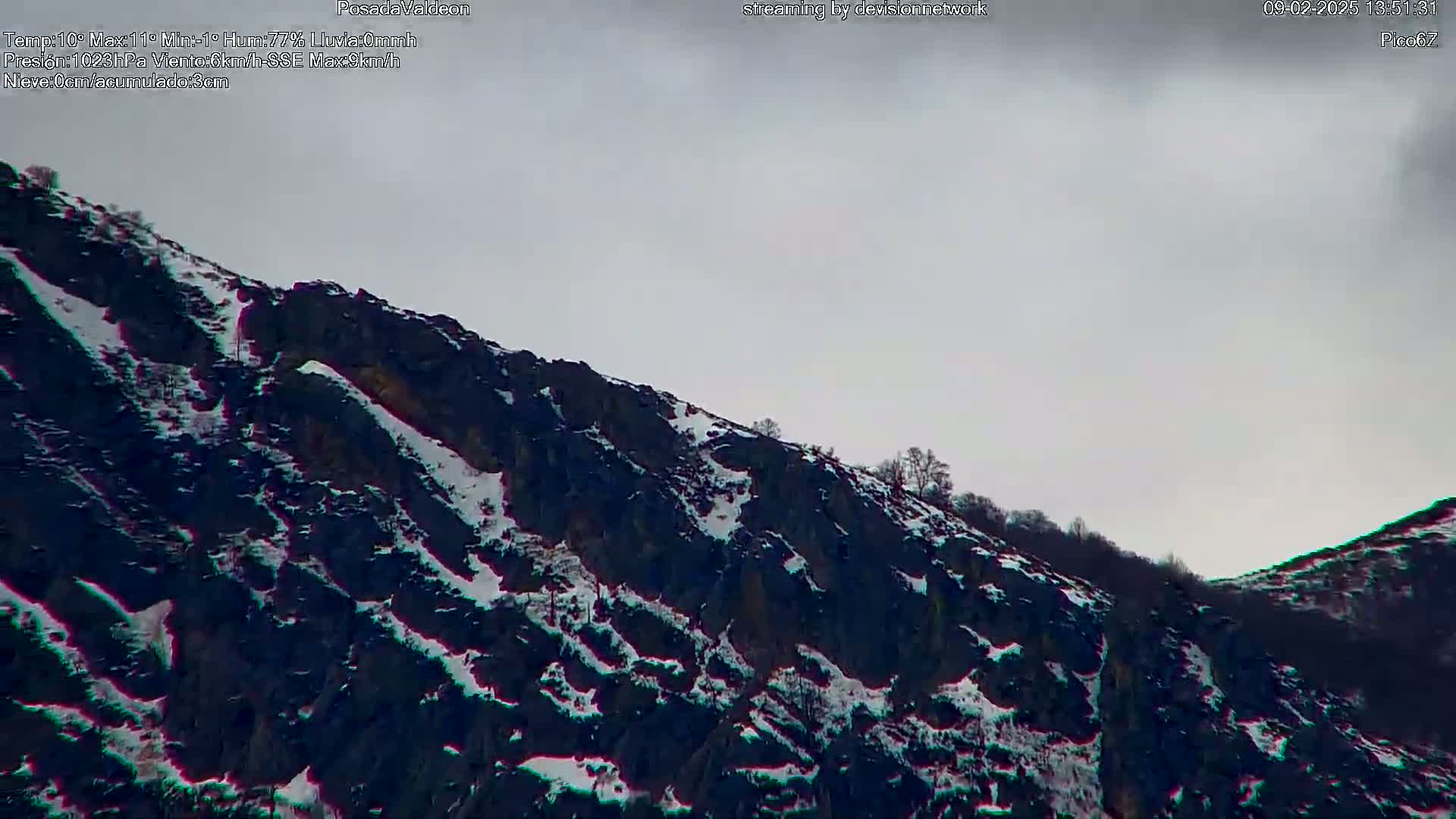 A snow-dusted, dark mountainside under a cloudy sky.