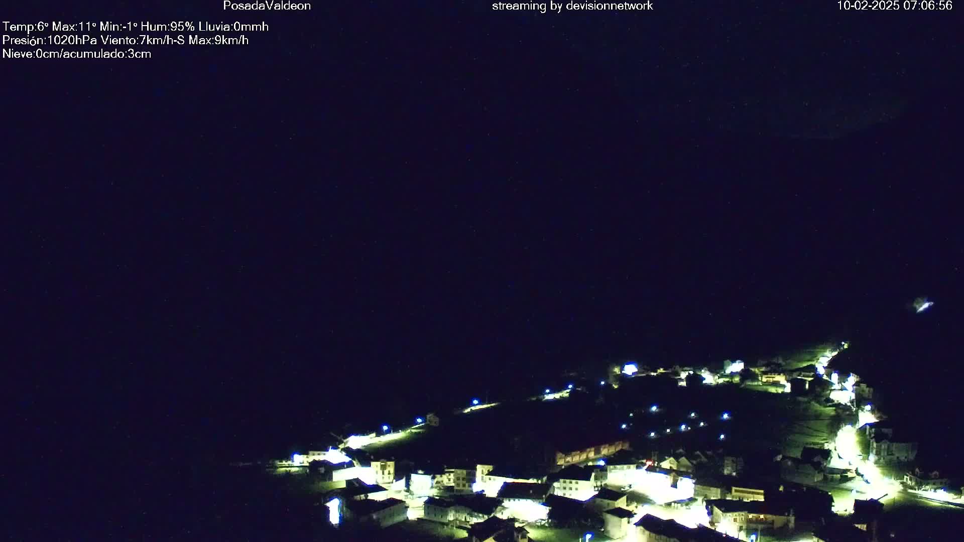 A small, illuminated village is nestled in a dark landscape under a clear night sky.