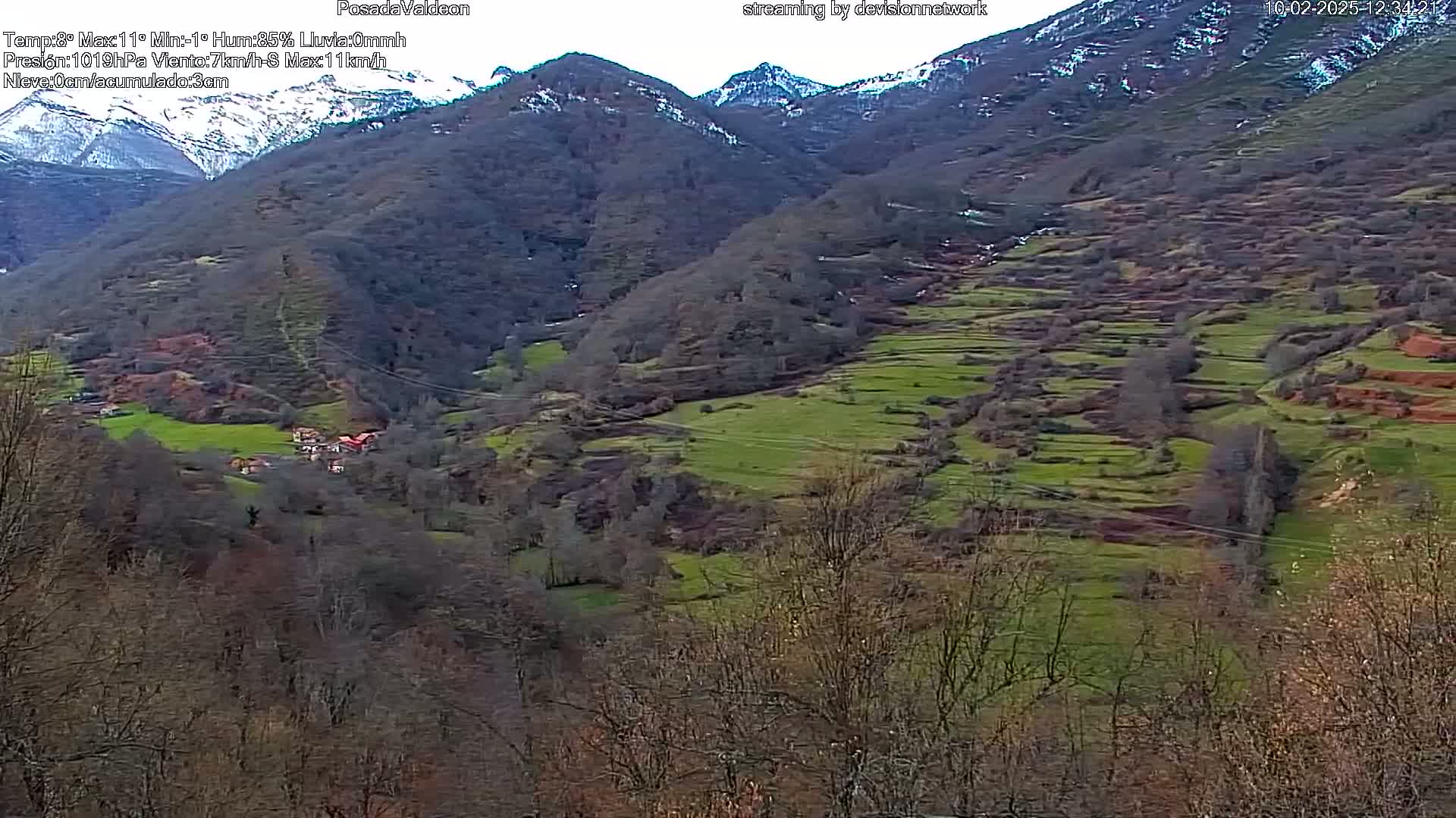 A mountainous landscape with terraced fields, a small village nestled in the valley, and snow-capped peaks in the background under an overcast sky.