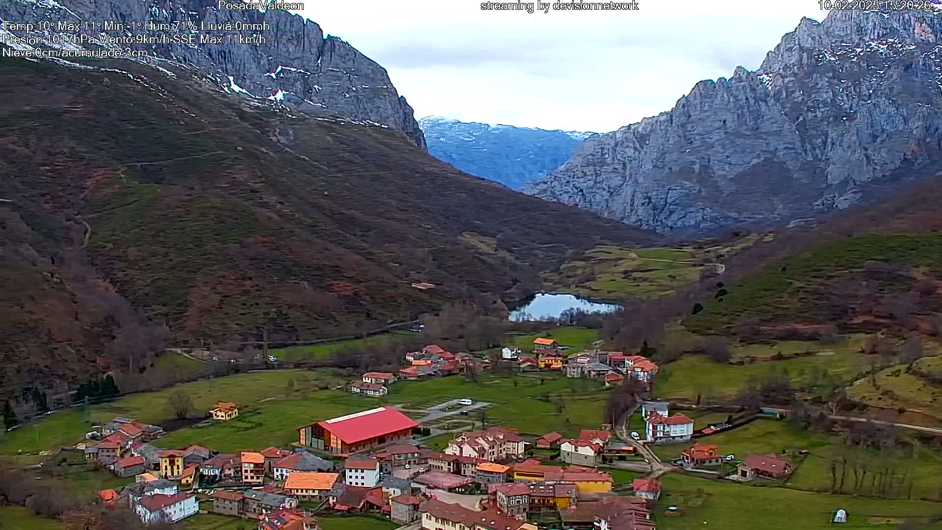 A small village nestled in a verdant valley between towering, snow-dusted mountains under an overcast sky.