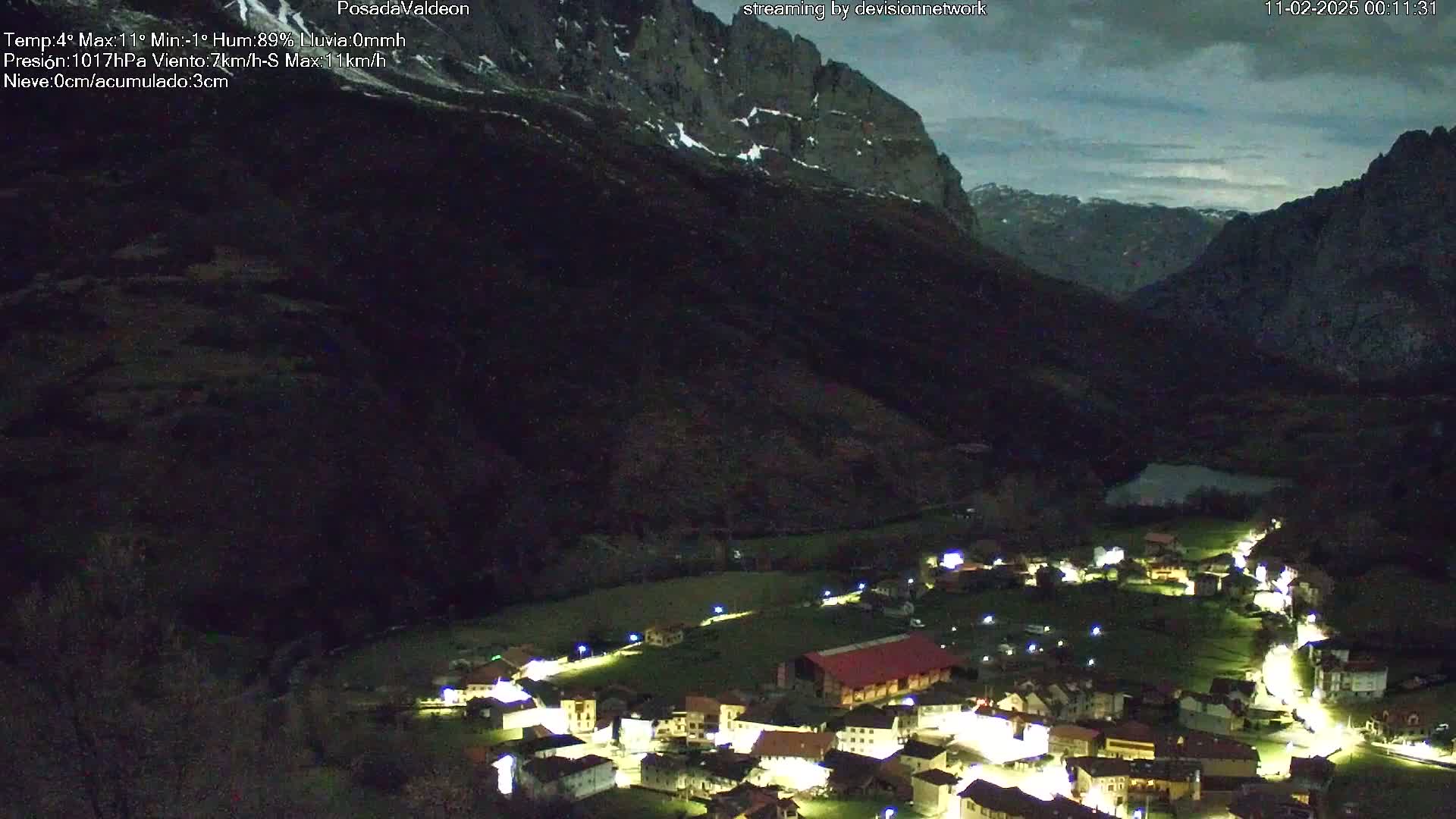 A small, illuminated village nestled in a dark valley between snow-capped mountains under a twilight sky.