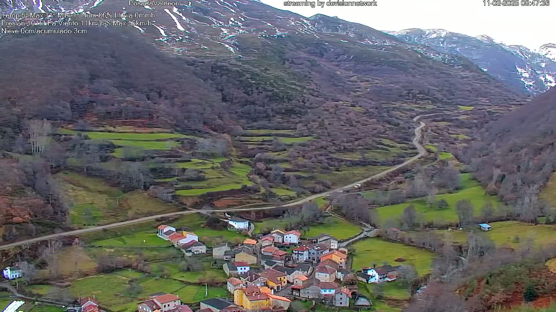 A small village nestled in a valley between snow-dusted mountains, with a winding road leading to it.