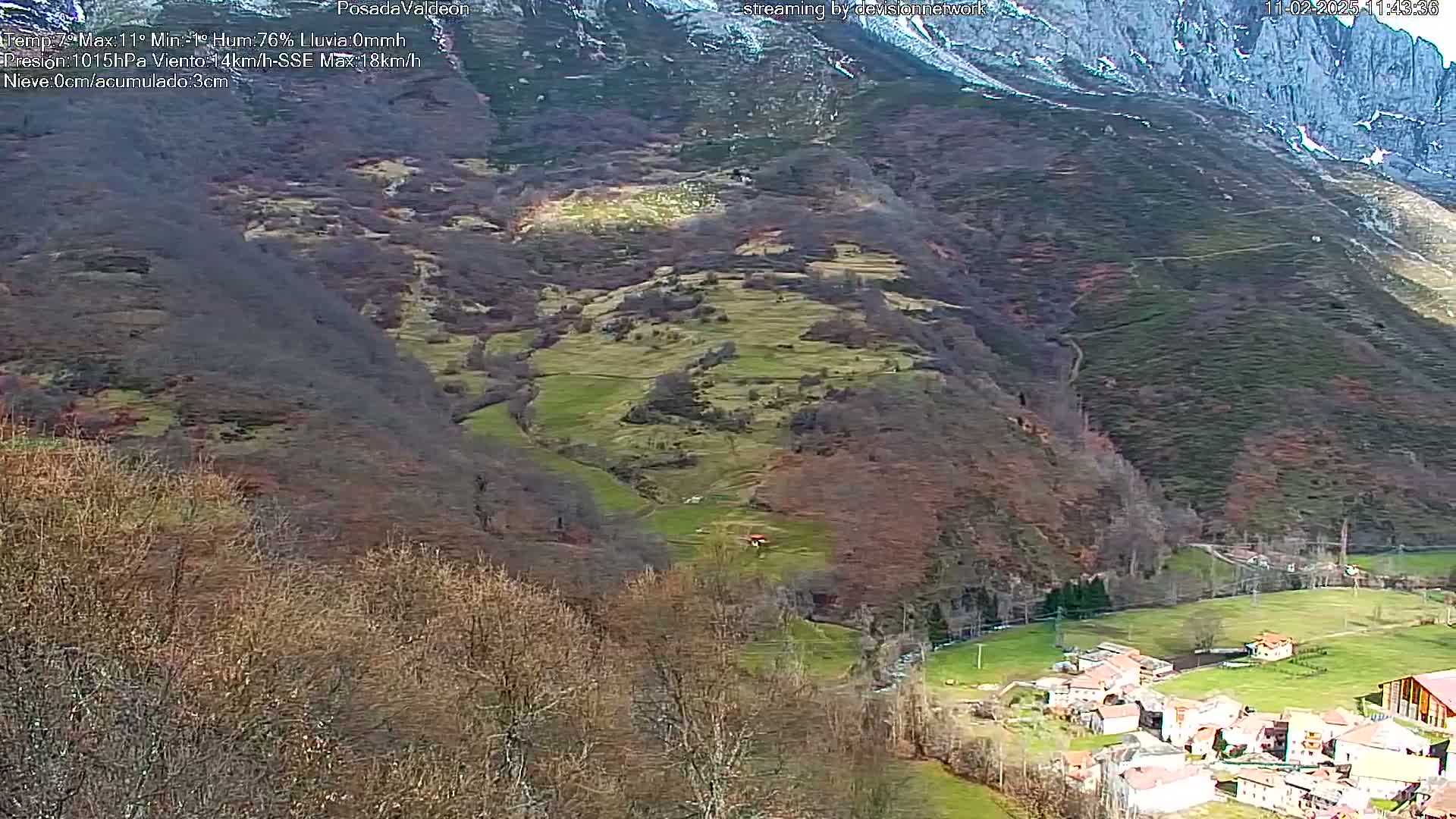 A high-angle view shows a valley village nestled amongst brown, sparsely wooded hills and mountains under a mostly clear sky.