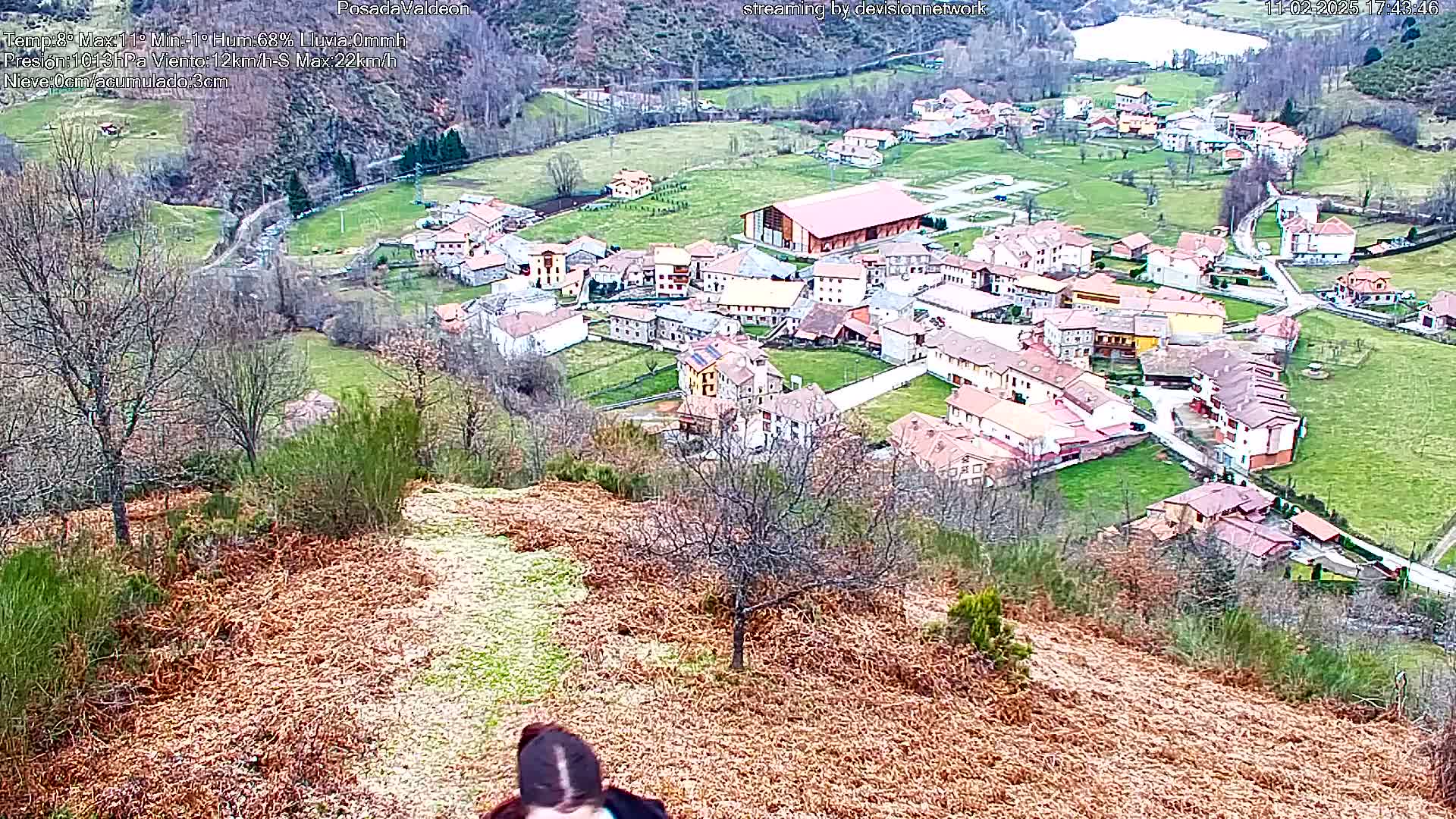A high-angle view shows a small village nestled in a valley, surrounded by brown, grassy hillsides under a seemingly clear sky.