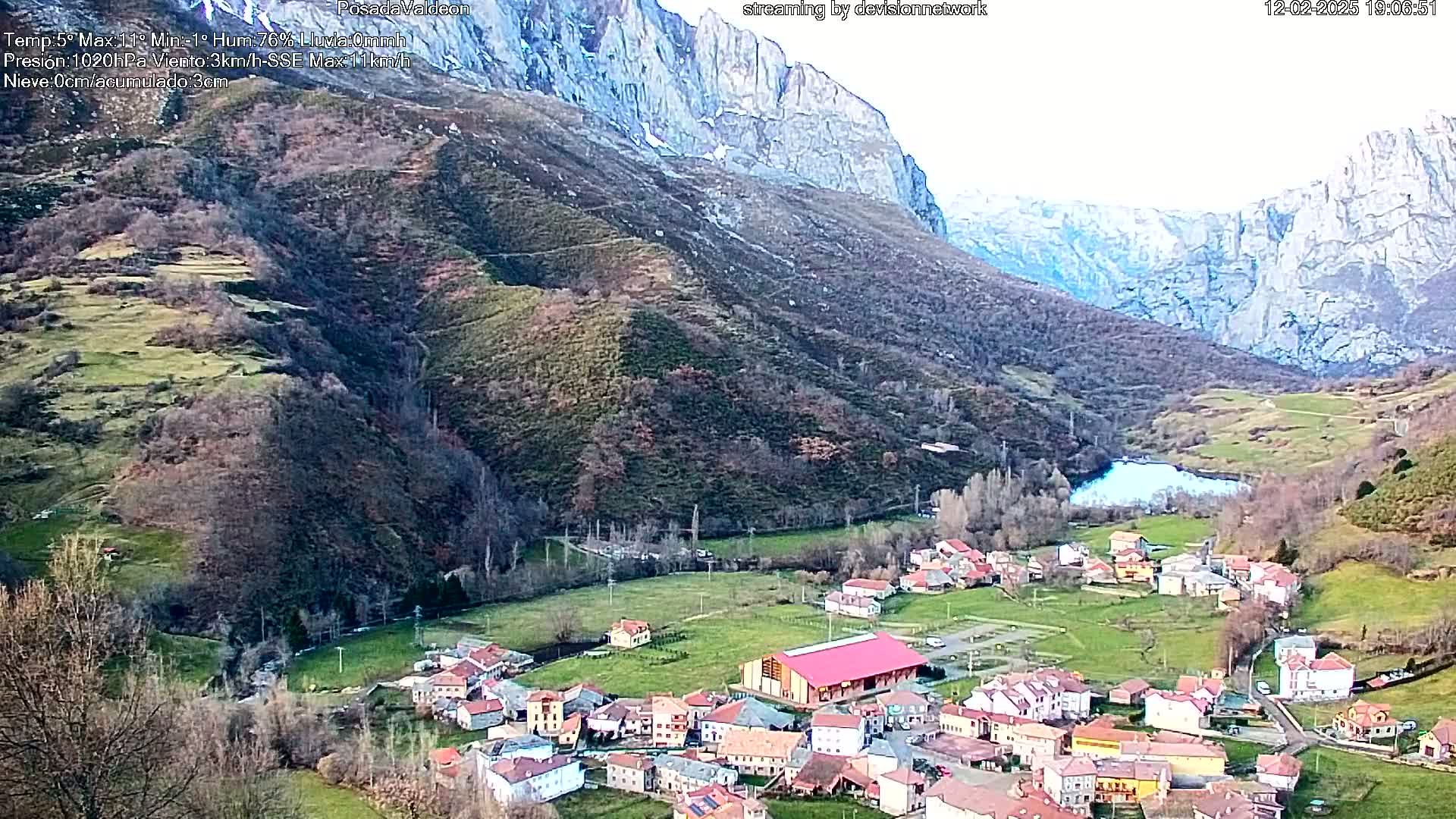 A small village nestled in a valley between towering, snow-dusted mountains under a mostly clear sky.