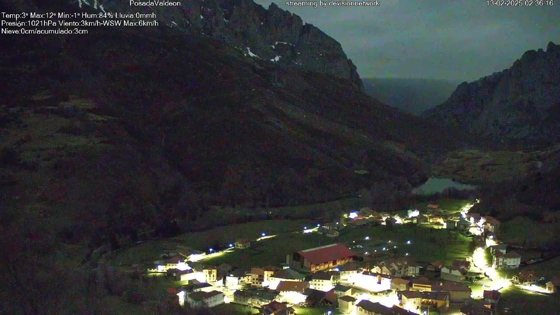 A small village nestled in a valley between dark mountains at night, under a cloudy sky.