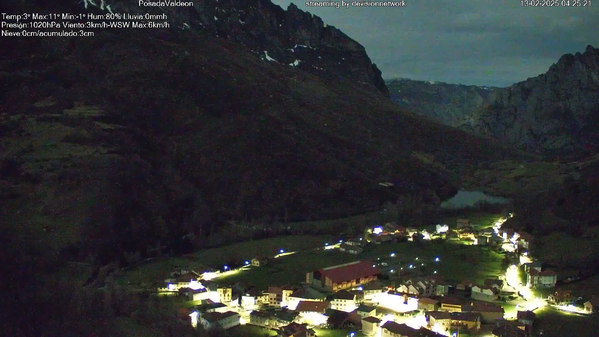 A nighttime, aerial view of a small village nestled in a valley between dark mountains under a mostly clear, twilight sky.