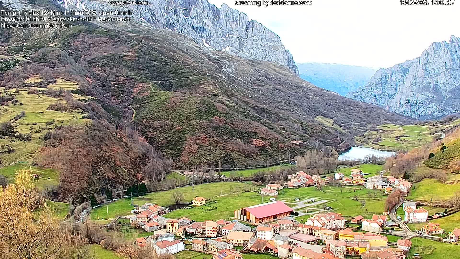 A small village nestled in a valley between mountains, with a lake visible nearby, under a mostly cloudy sky.