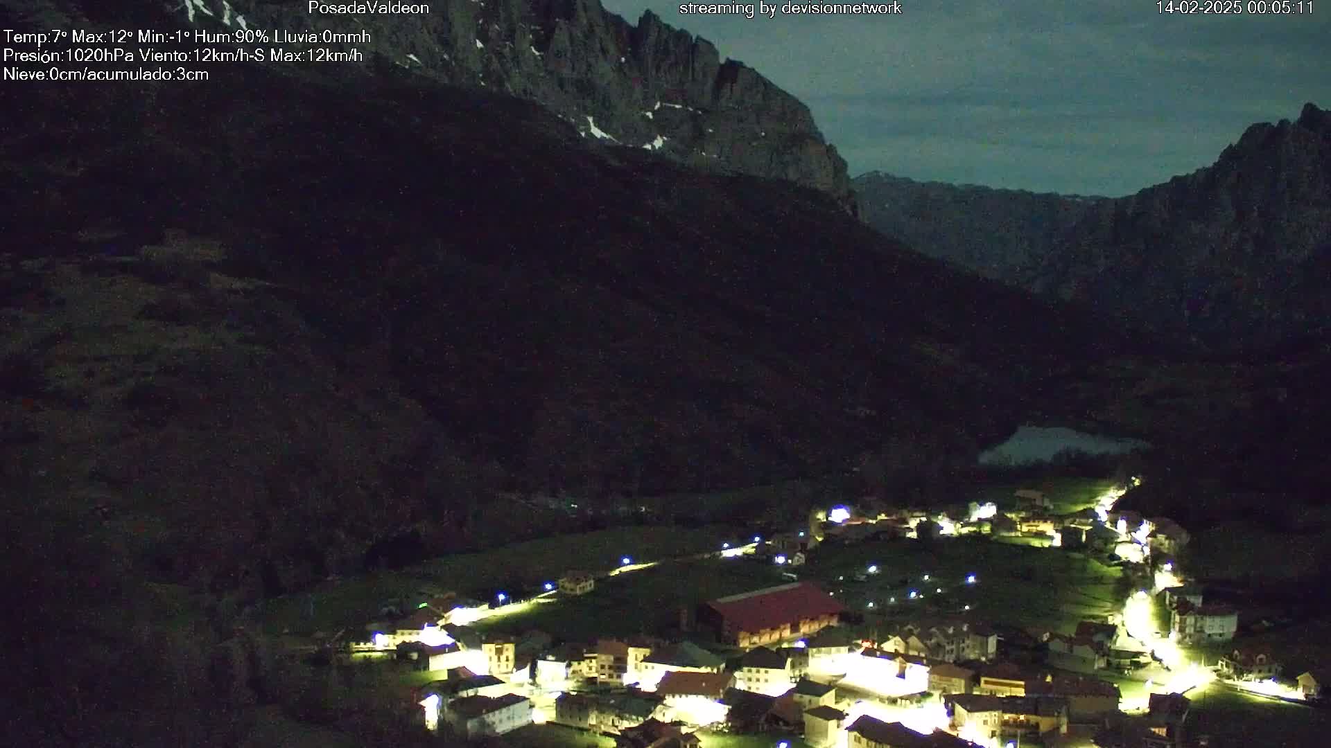 A nighttime view of a village nestled in a valley between dark mountains under a mostly clear, dusky sky.