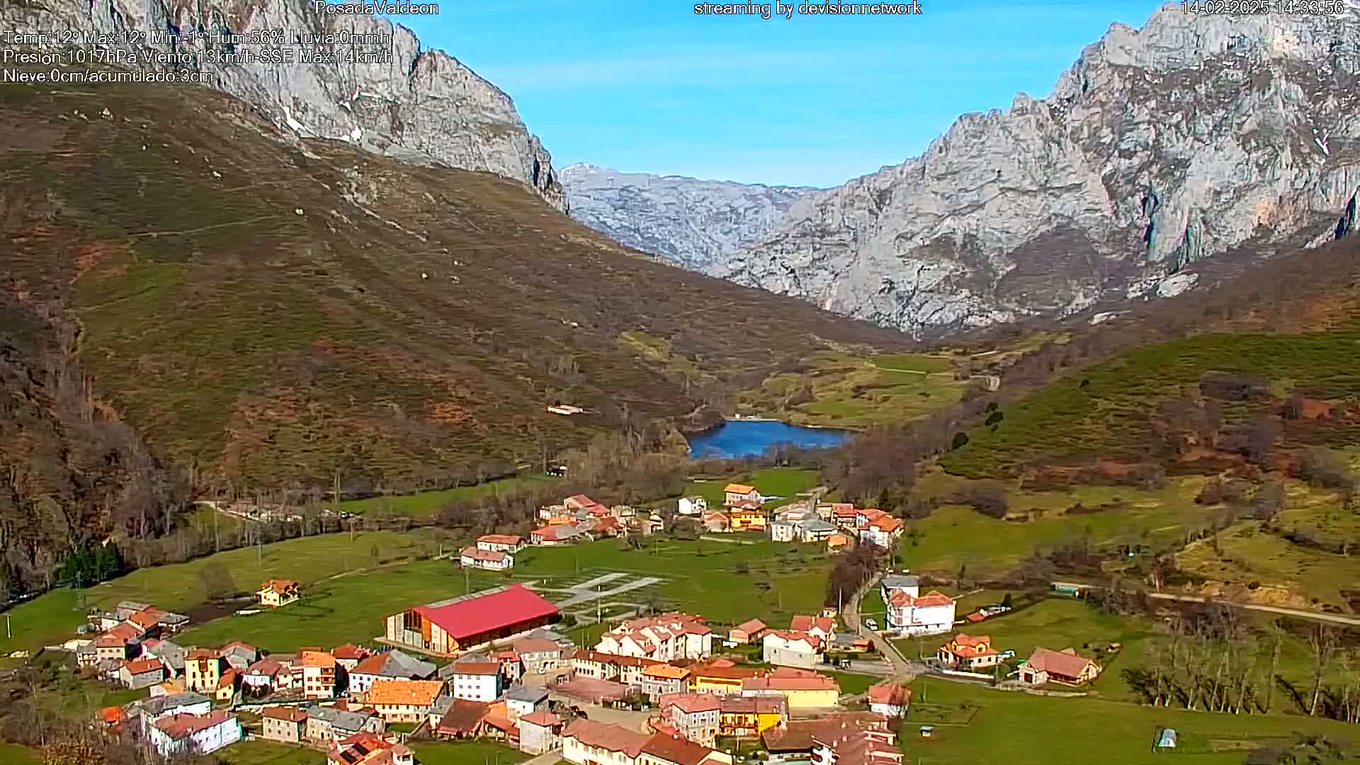 A small village nestled in a valley between towering, snow-dusted mountains on a sunny day.