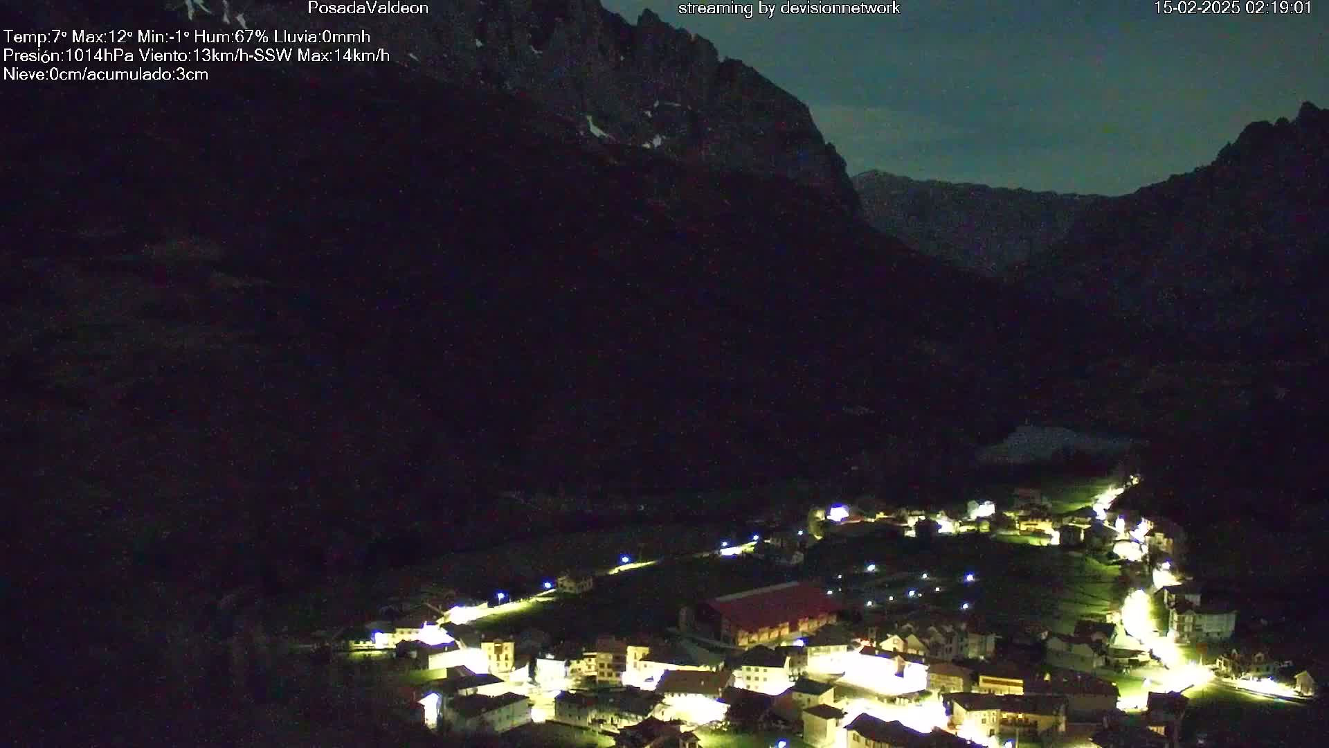 A small village nestled in a valley at night, illuminated by lights, with mountains in the background under a dark sky.